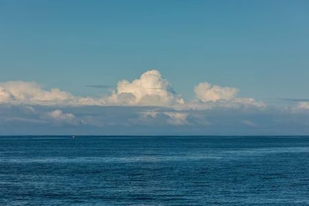 Calm blue ocean stretching to the horizon under a clear pale sky with scattered clouds